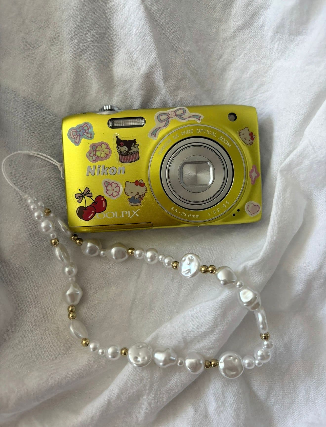 A yellow camera decorated with stickers and a pearl strap